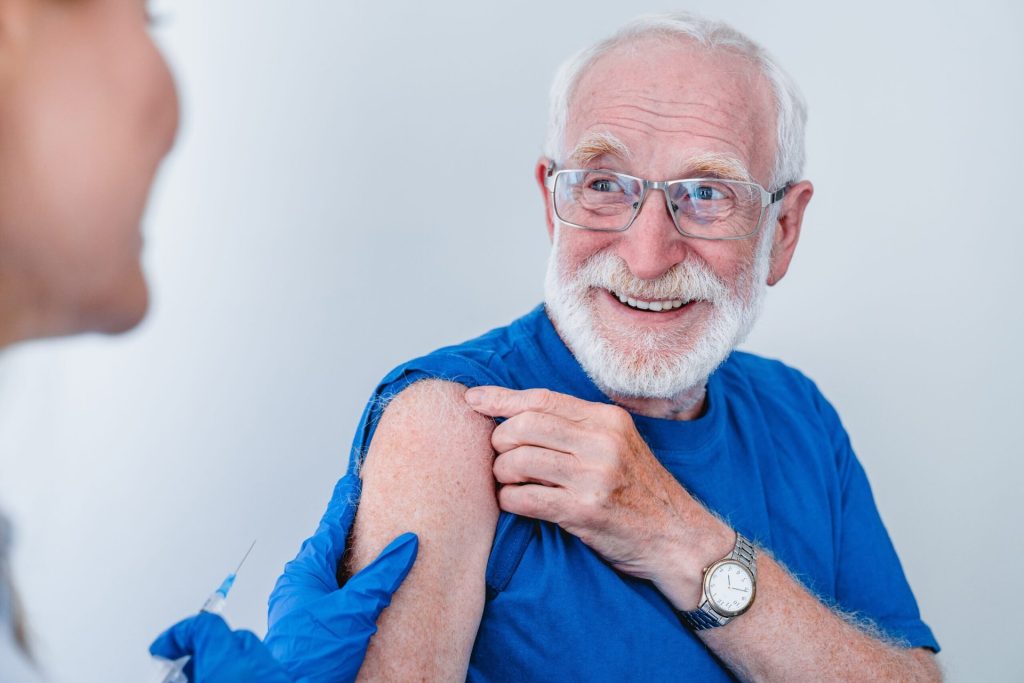 Smiling older man getting a flu shot from a doctor or pharmacist.