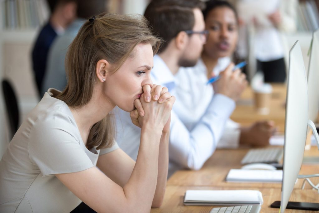 Unhappy worker at a computer in an office with coworkers in the background