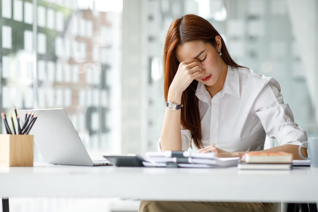 Stressed businesswoman working in an office at her desk with a laptop and a headache or feeling of tiredness