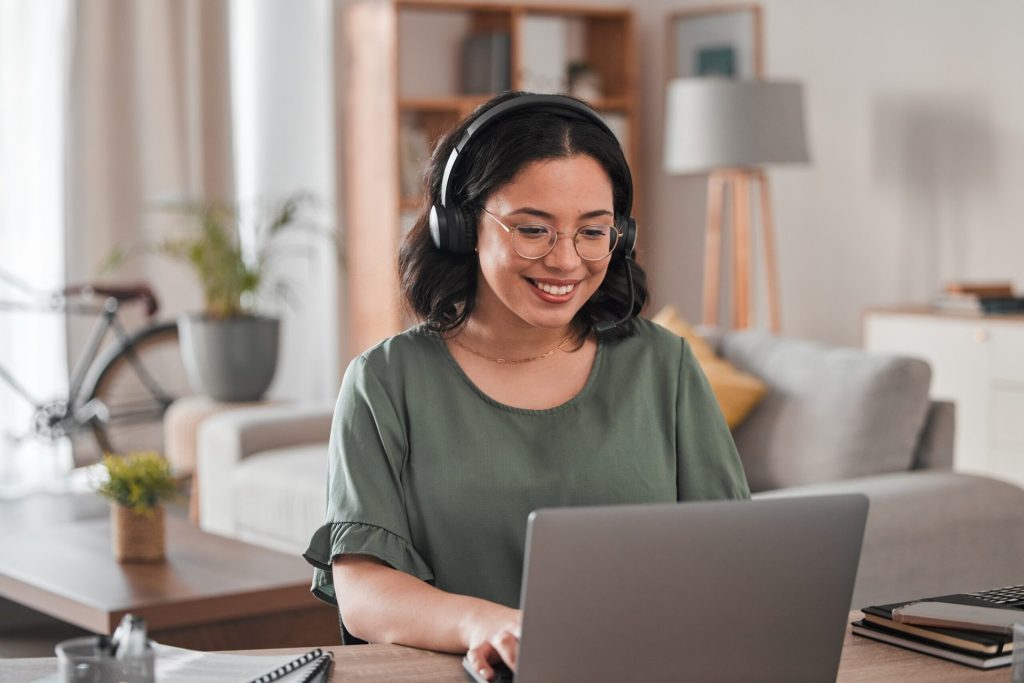 Happy, smiling woman working on a laptop, wearing headset. Virtual assistant.