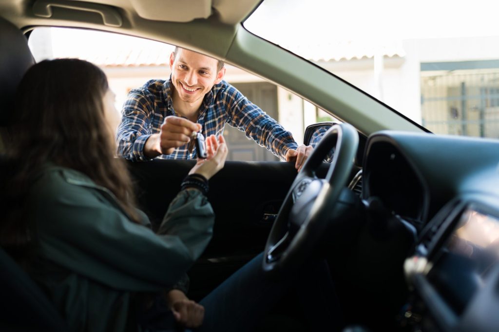 Father smiling and giving his teen daughter the car keys. Adolescent girl ready to start driving after getting her driver's license.