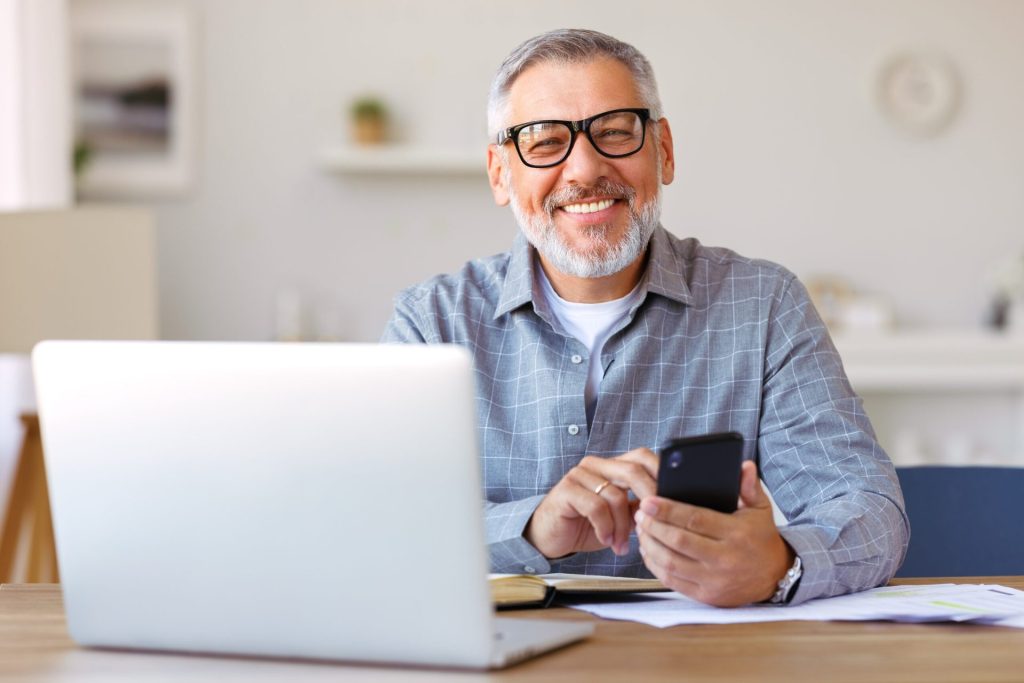 Happy senior man working on his laptop and phone at a remote job.