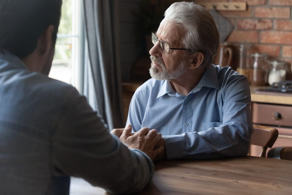 Senior man with Alzheimer's, memory disorder comforted by adult son.