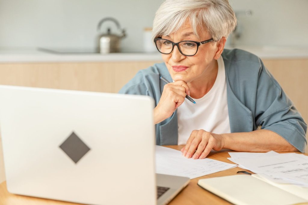 Senior woman using a laptop and writing notes