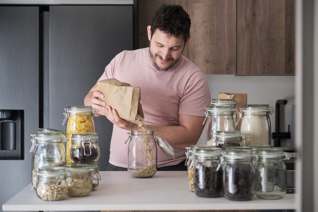 Young man filling up a jar with oats from a paper bag. Bulk food storage.