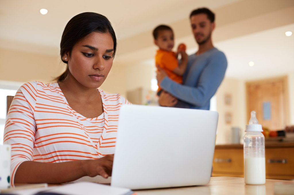 Working mother with dad and baby in the background
