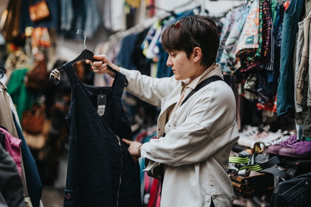 I Thrift Shop for a Living. Here Are My 8 Best Tips for You. A person shopping in a thrift store, examining a secondhand black dress.