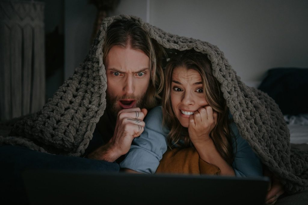 This Is America’s Favorite Scary Movie in 2025 Terrified young couple covered with blanket and watching a horror movie