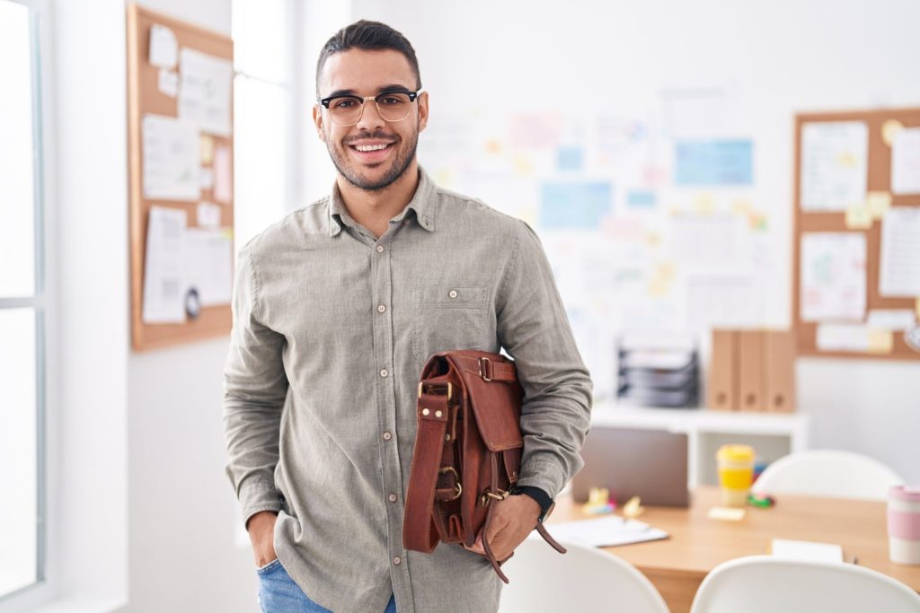 Young man smiling and holding a briefcase in an office