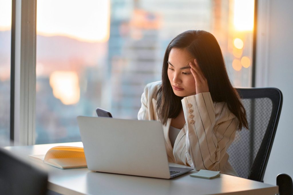 Worried woman with a smartphone and laptop at work